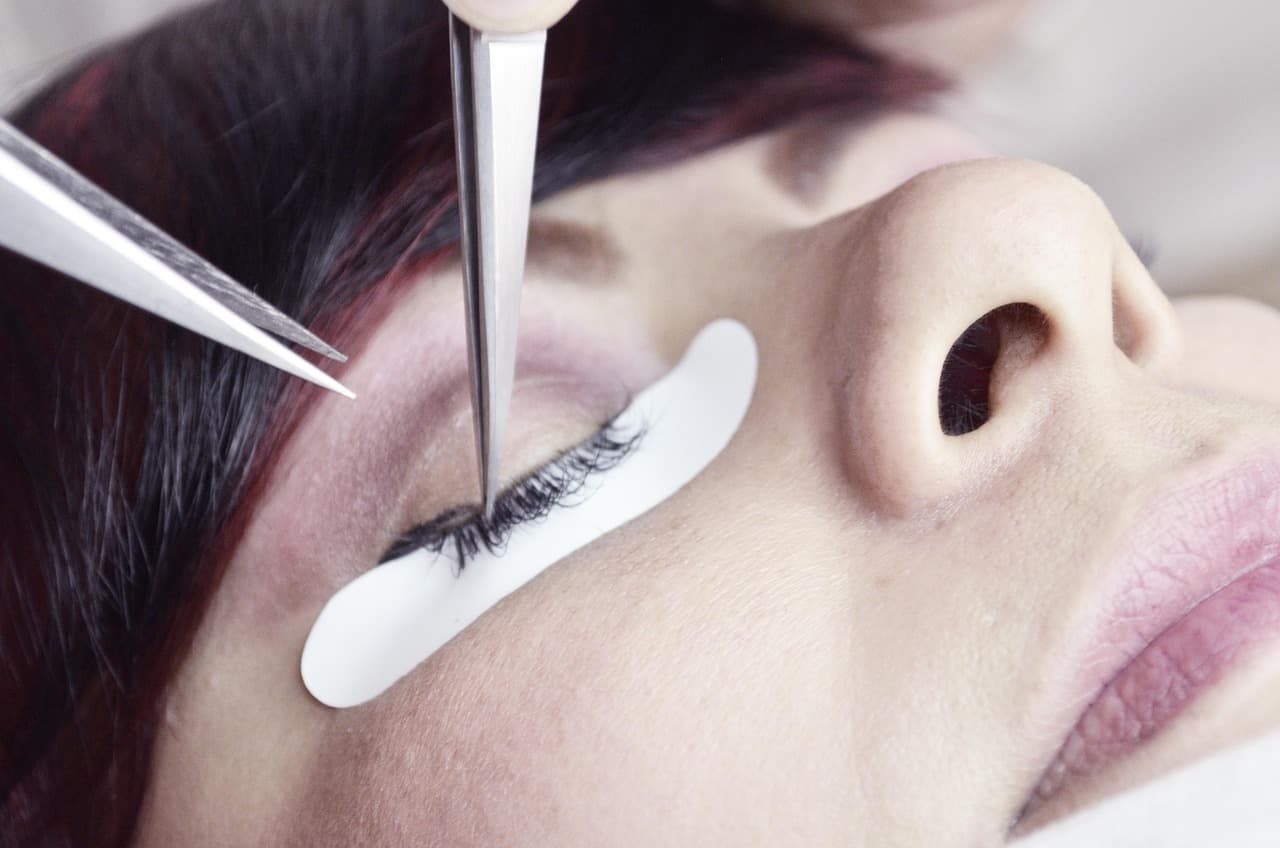Lashes being set one by one with fine tweezers, a pad under the lower lashes