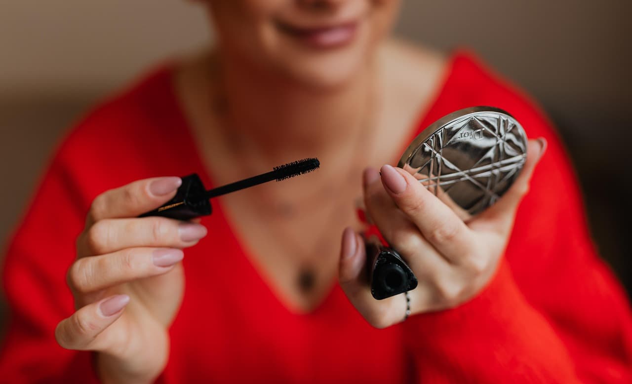 Mascara being brushed out of its tube, a compact in the other hand